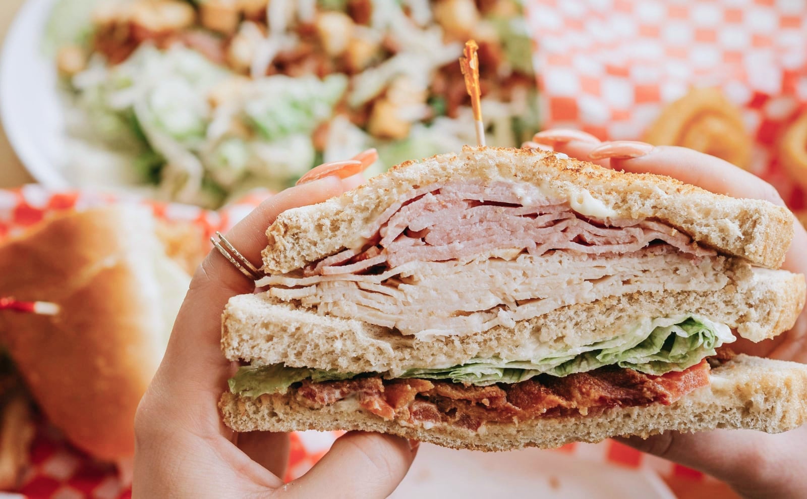 two hands holding half of a sandwich of white bread with turkey, bacon, lettuce, and mayo