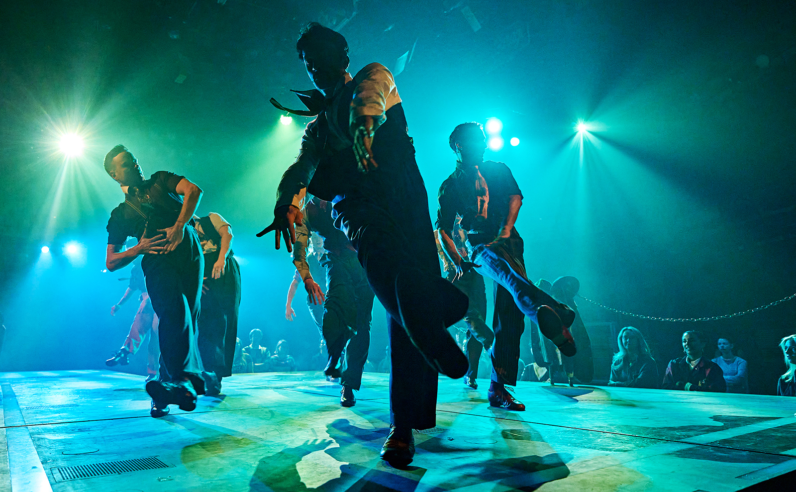 a group of men dancing on a stage wearing shirts and ties with green lighting