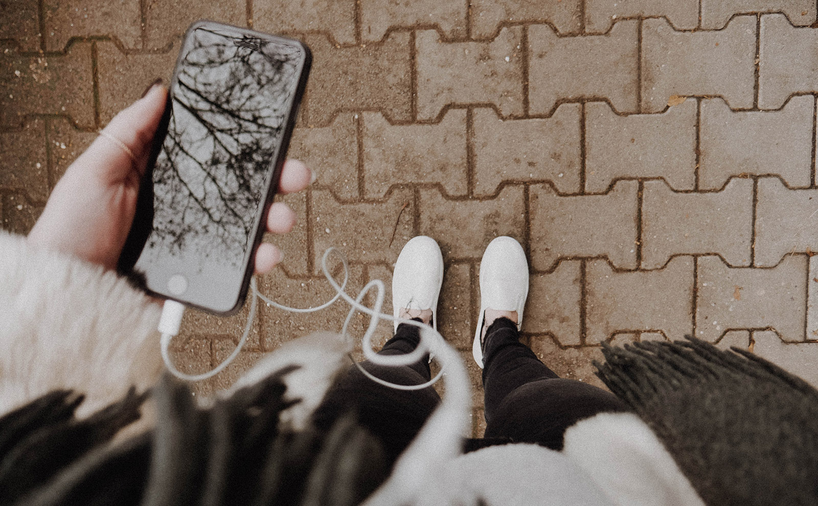 woman listening to headphones with a mobile phone standing on a cobblestone sidewalk