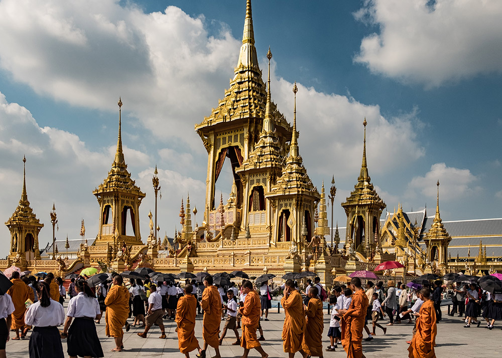monks in orange robes walking around the grand palace in bangkok on a sunny day