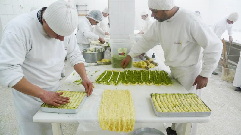 a long white table with phyllo dough and bakers in white hats