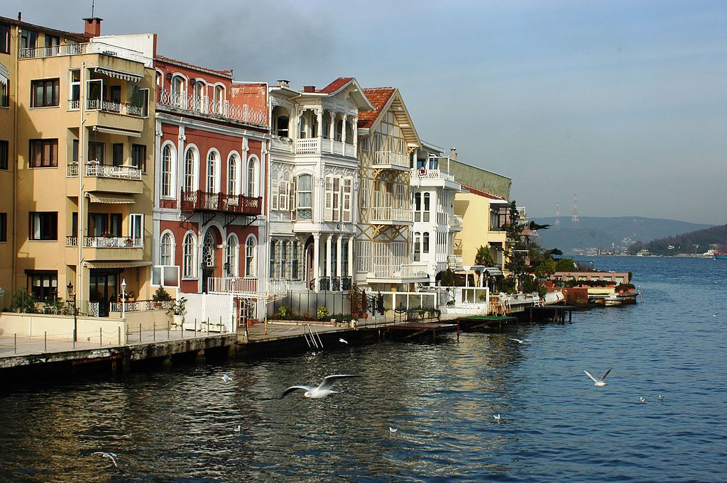 ornate white wooden house with four stories and small onion domes on the shore of the water