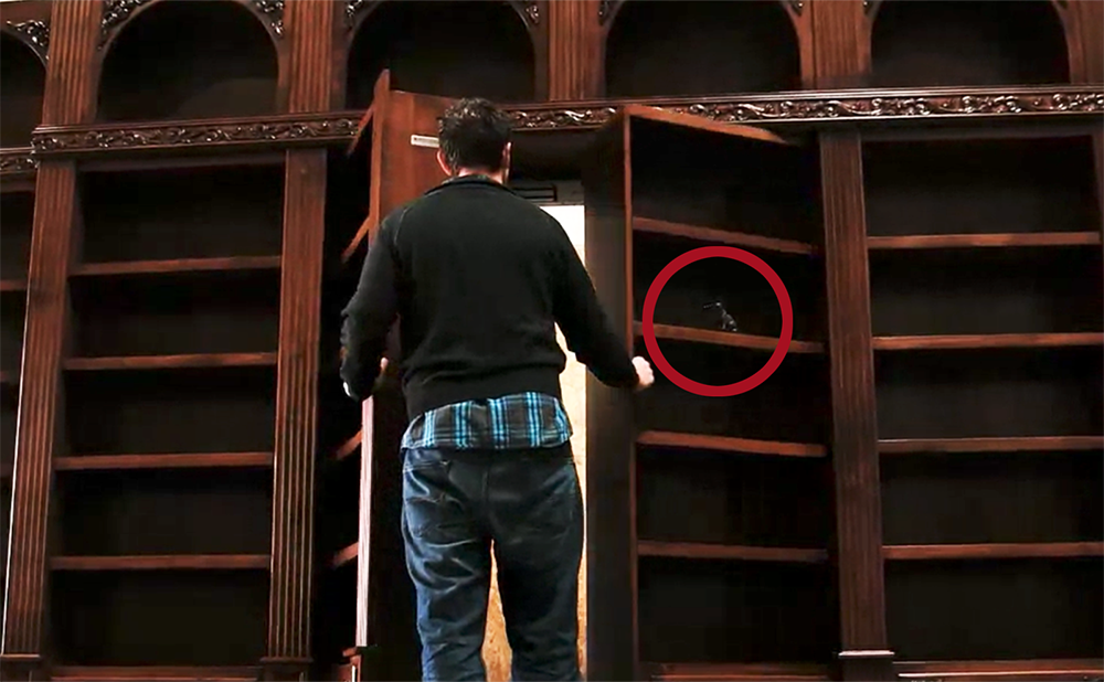 two wooden bookshelves opening up like a door with a man walking through them
