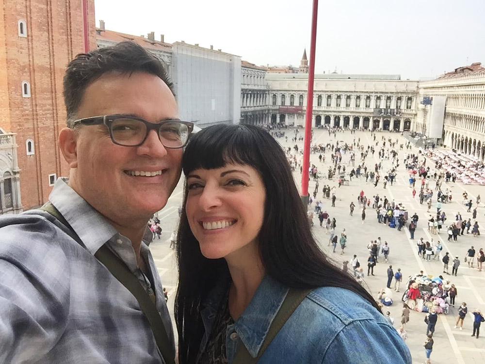  a man and a woman standing on a balcony overlooking st. mark's square in venice