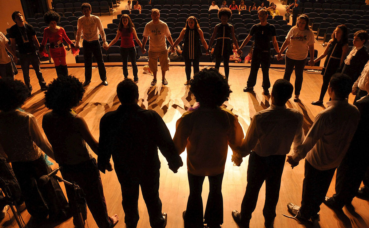 a group of actors standing in a circle on a stage holding hands