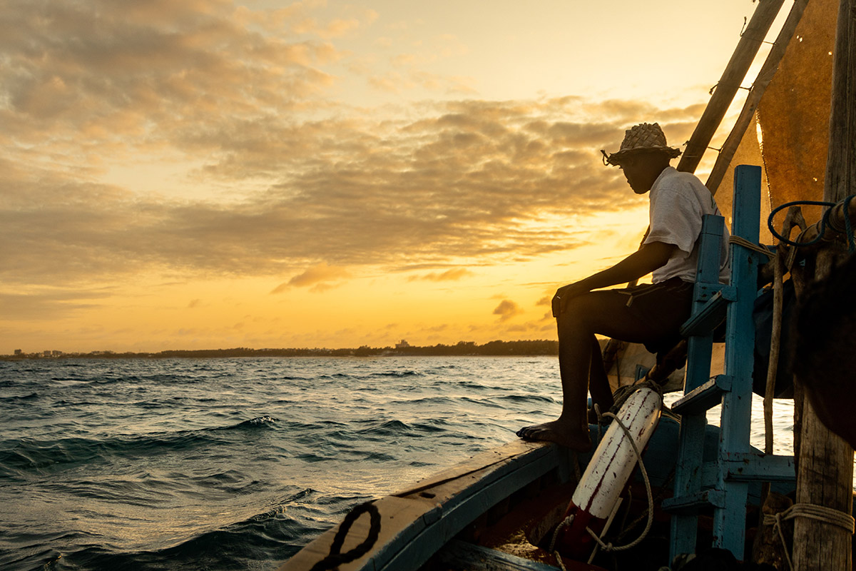 a man sitting on a boat at sea at sunset