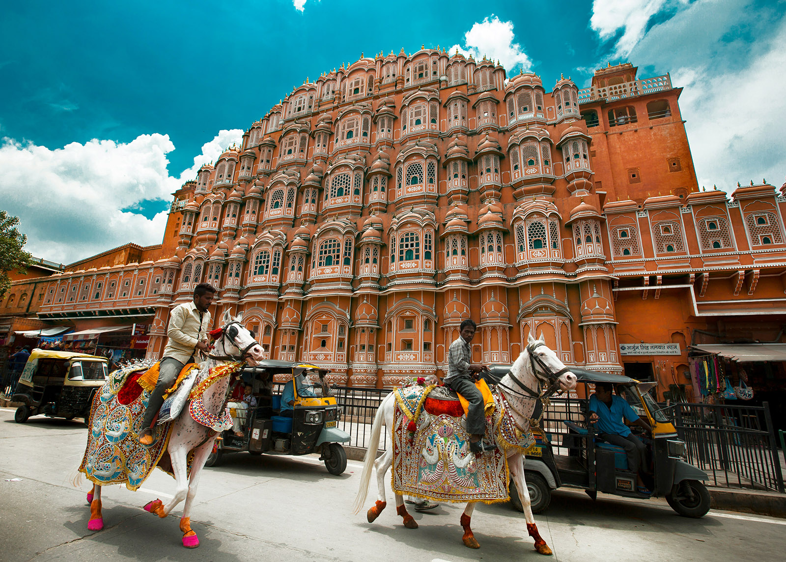salmon colored building in jaipur, india with two white horses in sparkly costumes in front