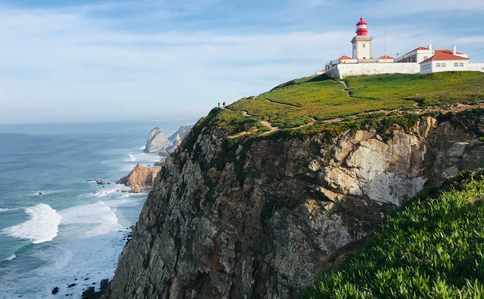 a red and white striped lighthouse on the edge of a cliff overlooking the atlantic ocean on a sunny day
