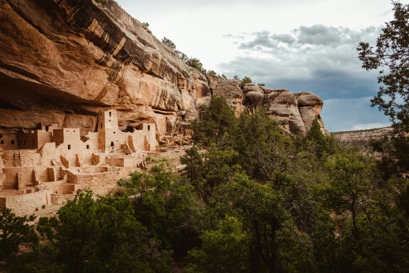 square pueblo houses built into the rust-colored rocks surrounded by green trees