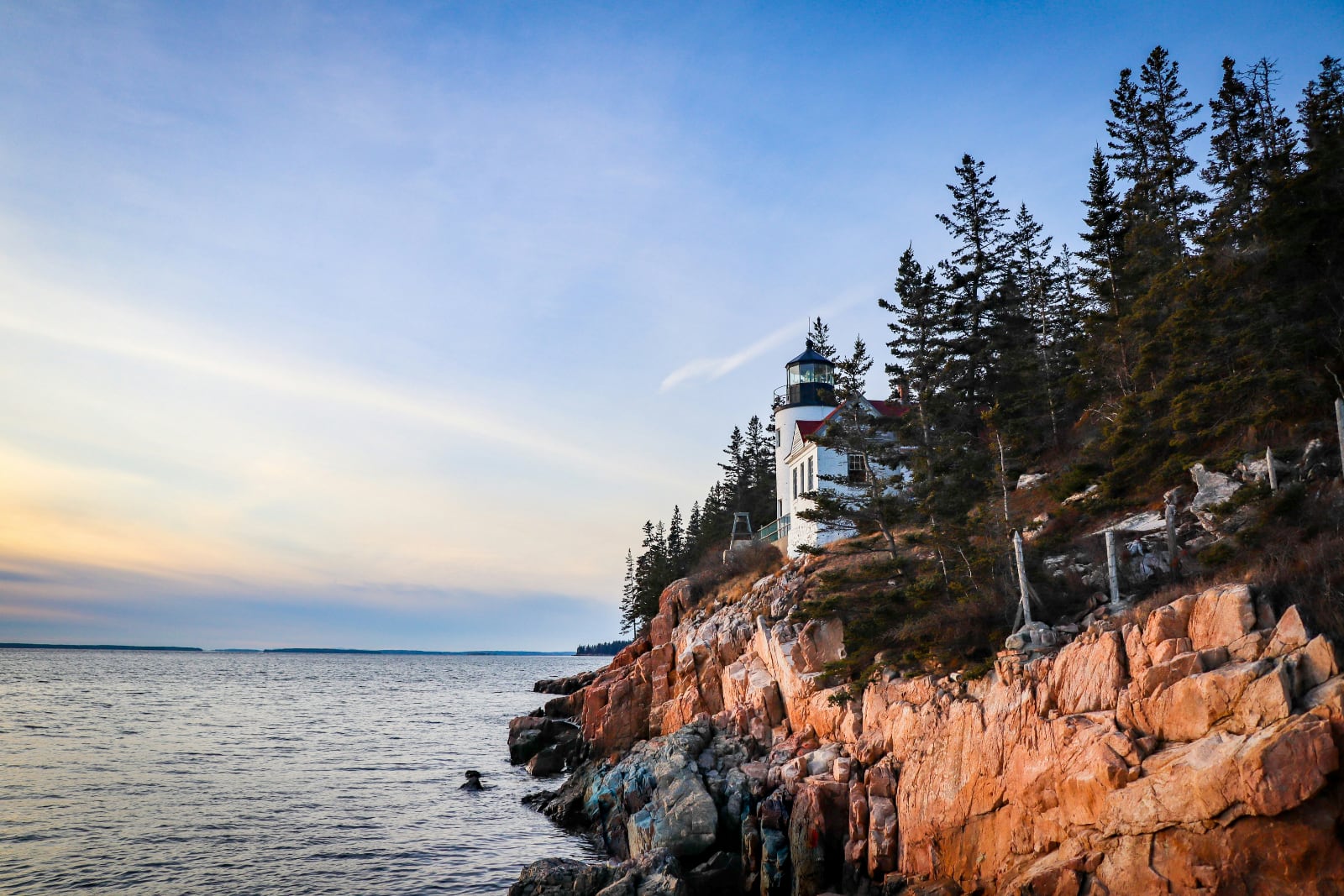 white lightouse on a red rock cliff overlooking the ocean