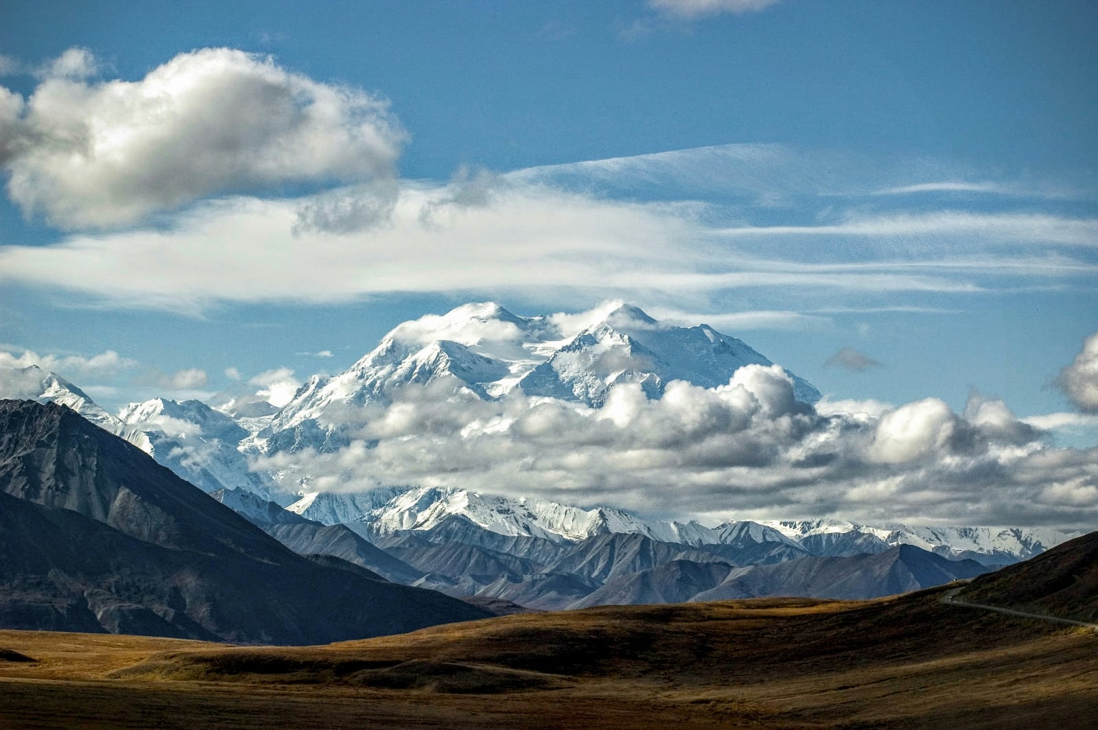 an enormous snow-capped mountain in the background with brown grassland in the foreground all under a bright blue sky
