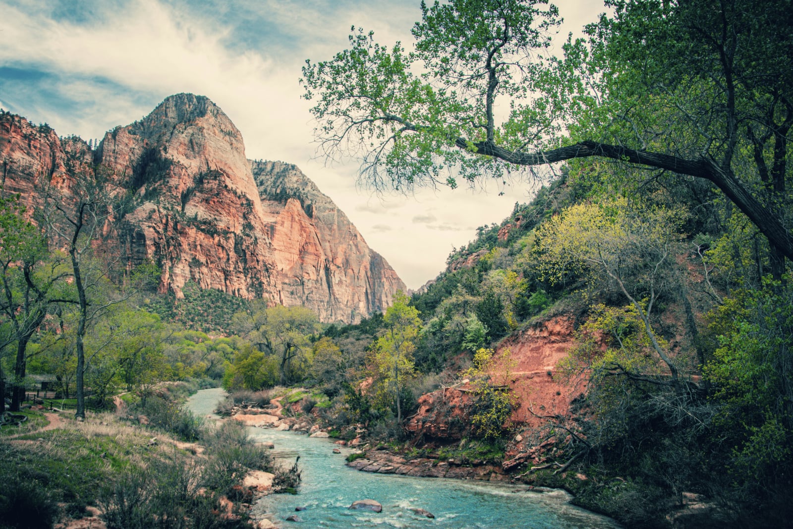 a turquoise blue stream winds through red rocky hills dotted with green trees and there's an enormous red red mountain in the background