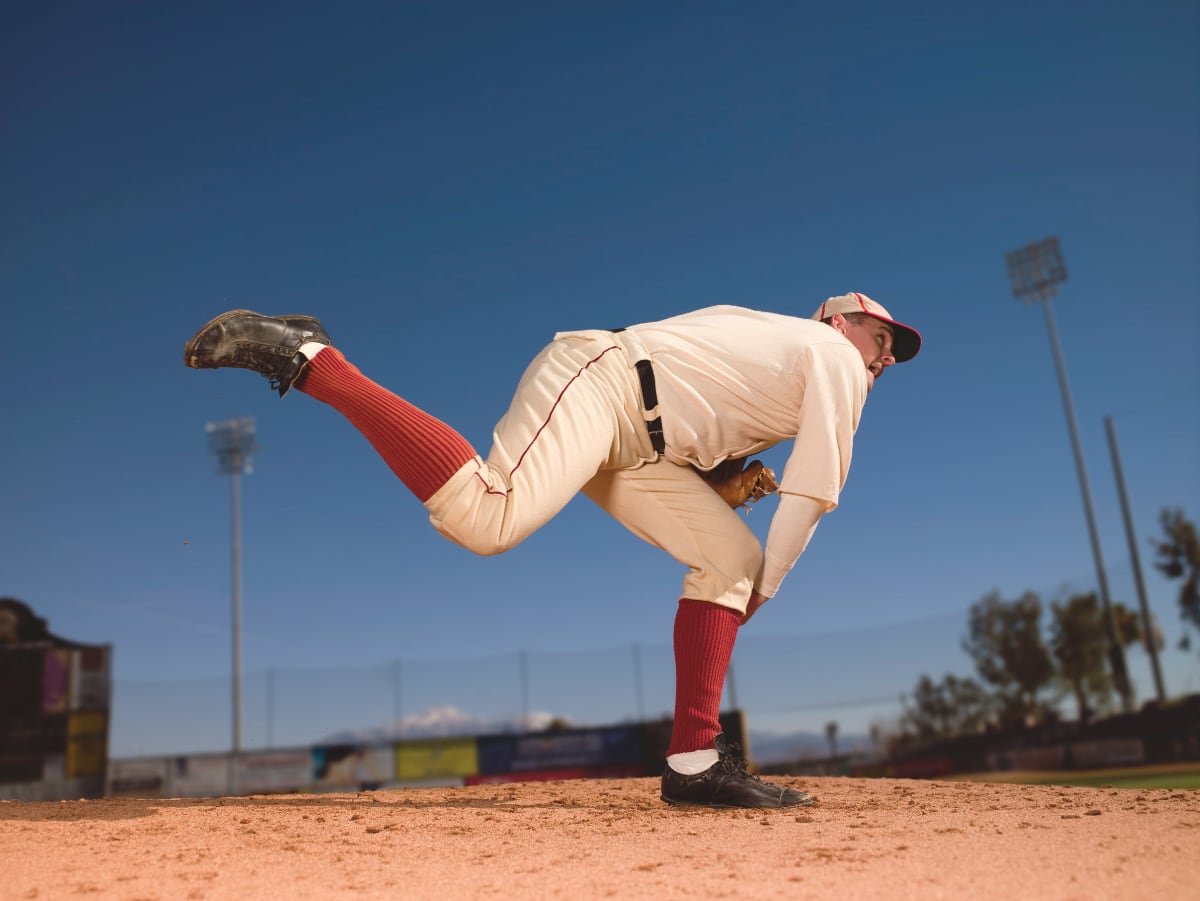 a pitcher leaning over on the mound to throw a baseball