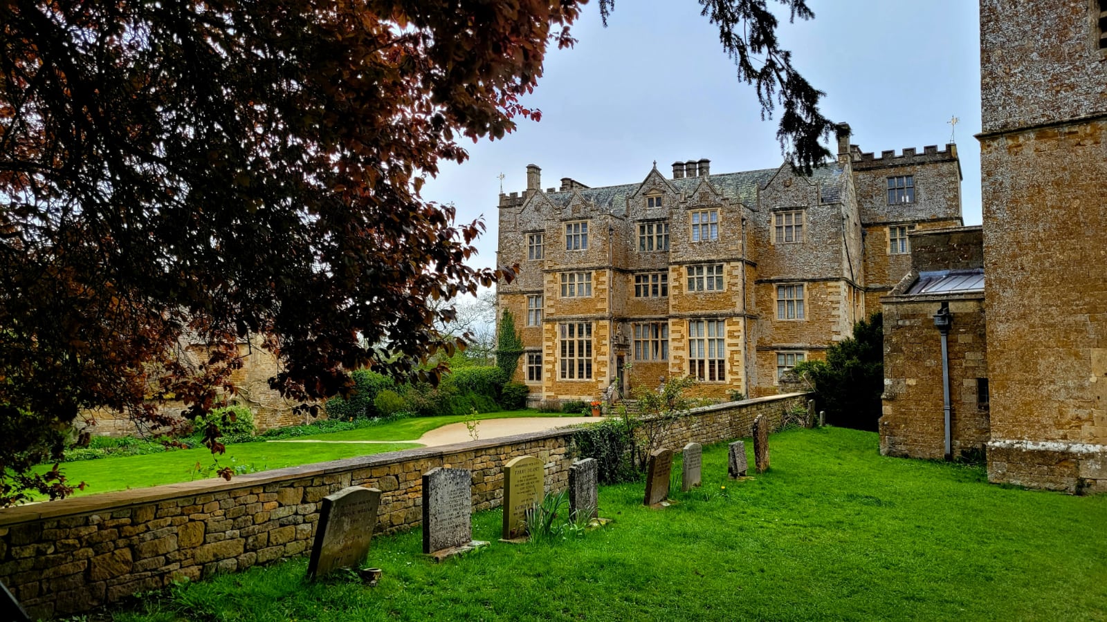 imposing yellow stone house with a dark green lawn and a row of very old headstones