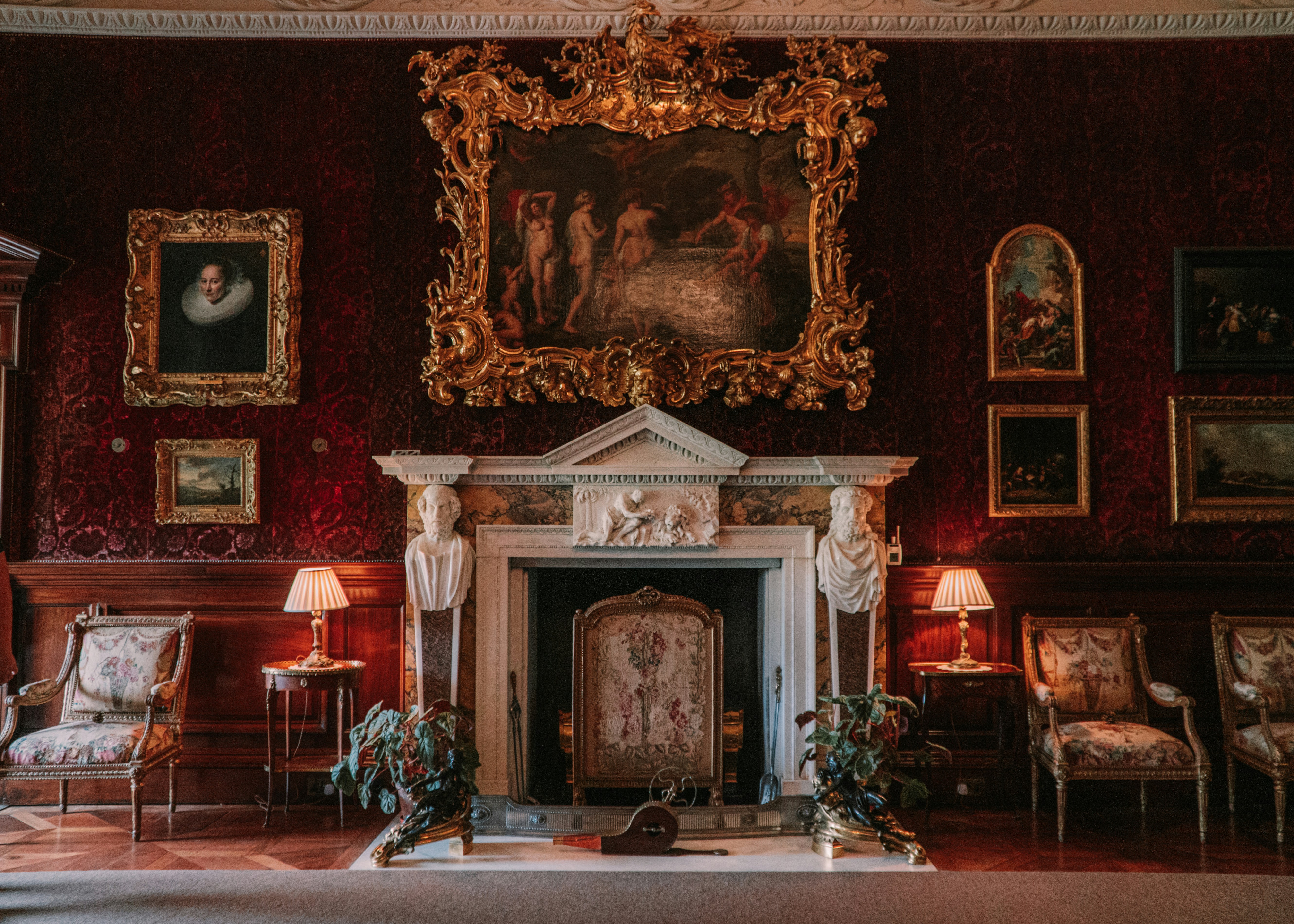 interior view of a sitting room with a baroque fireplace and red velvet wallpaper