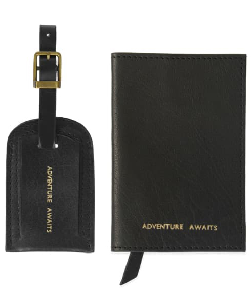 black luggage tag and passport cover stamped in gold with the words adventure awaits