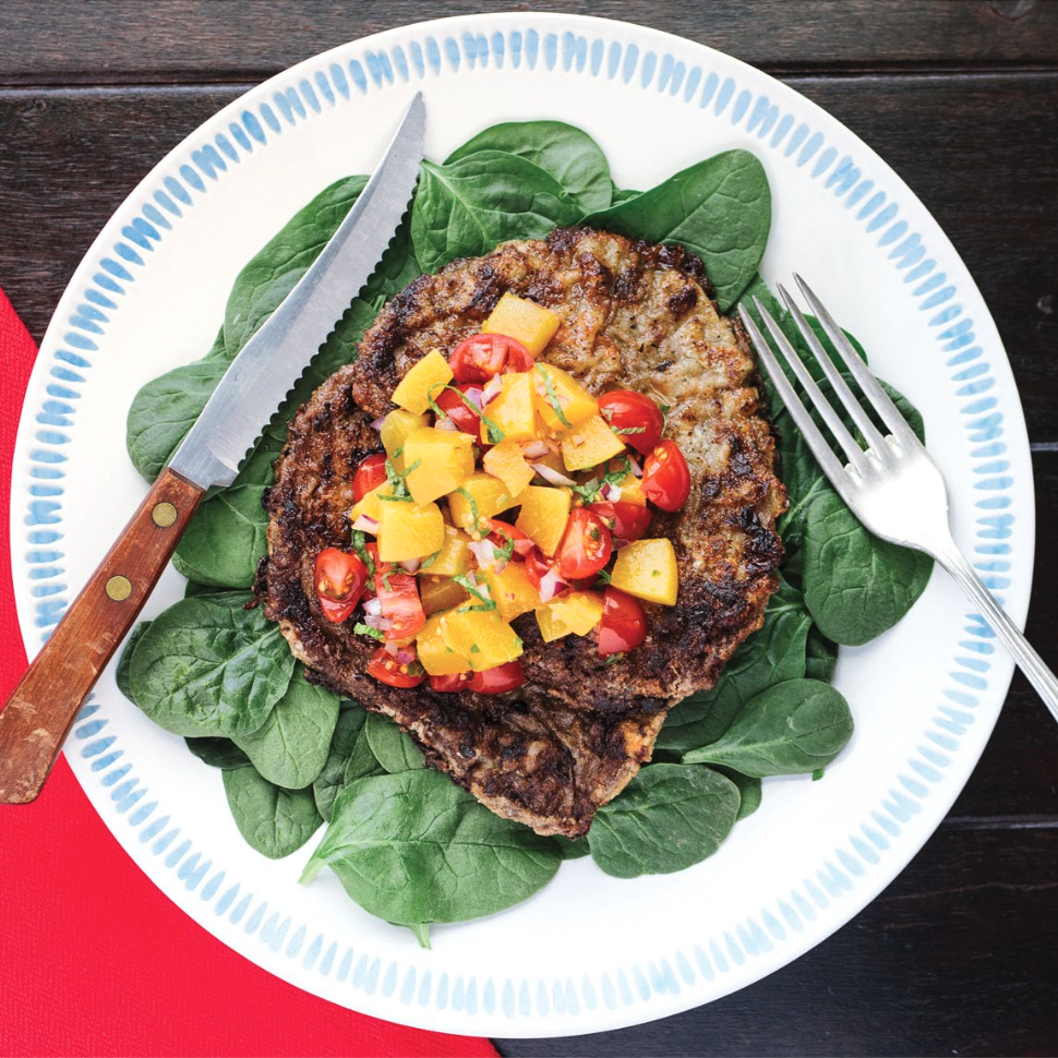  white plate with a close up milanesa cutlet on a bed of spinach with peach and tomato salsa on top