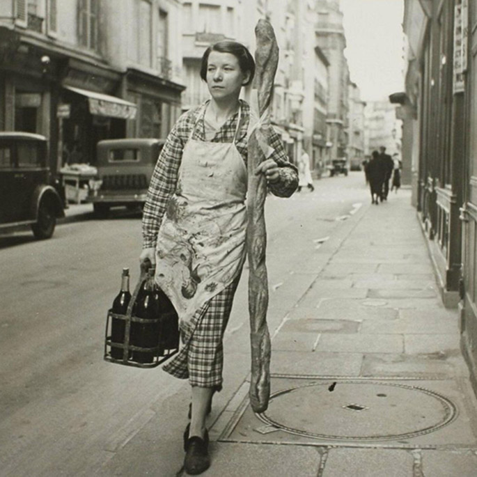 black and white photo of a french woman carrying a 6-foot long baguette on a paris street