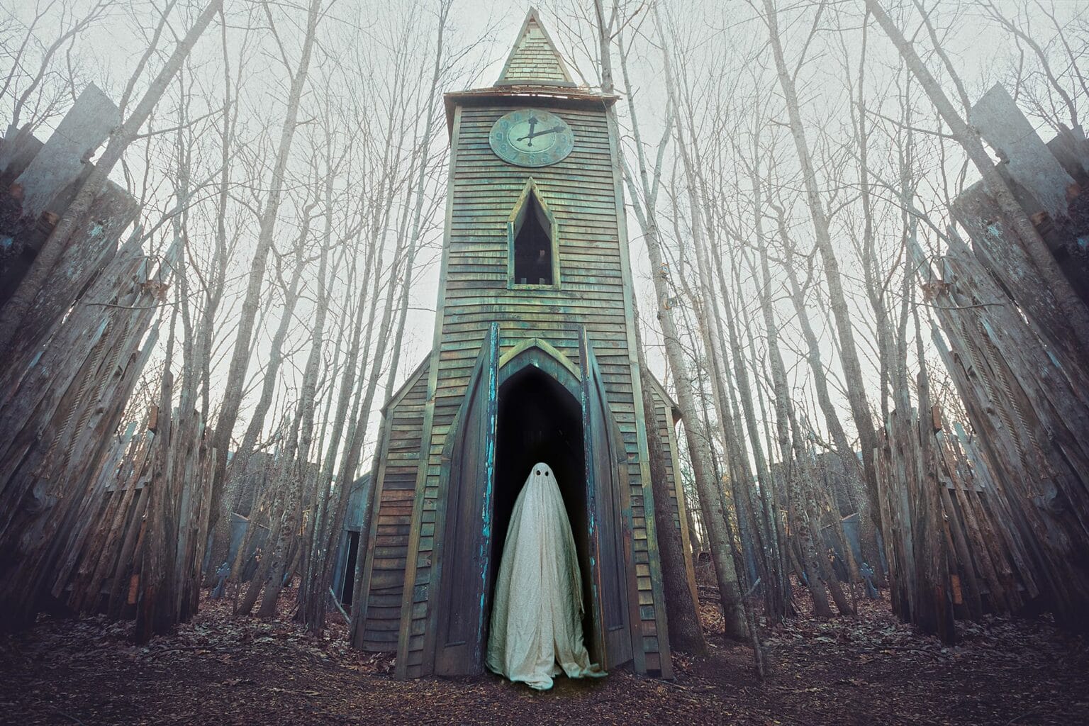 person in a sheet like a ghost standing in front of a crumbling building in the woods