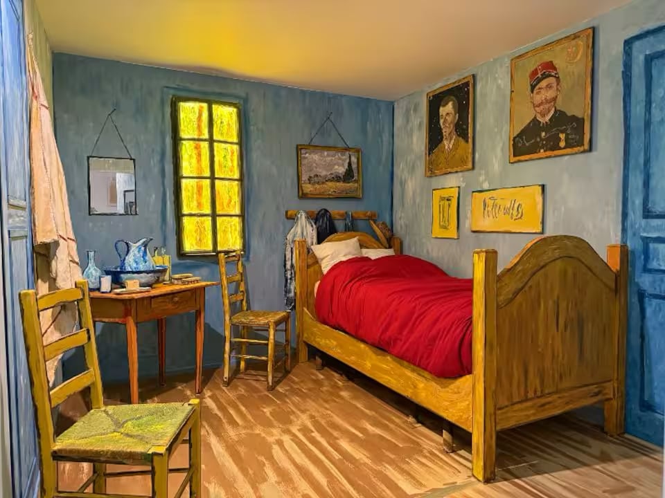 a bedroom that looks like a reproduction of van gogh's bedroom with yellow walls, a bed, and a straw-seated chair