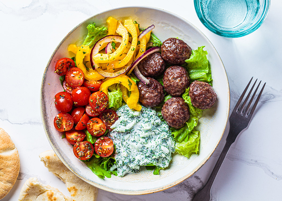 white plate on a table with meatballs, diced tomatoes, pepper strips, and yogurt sauce