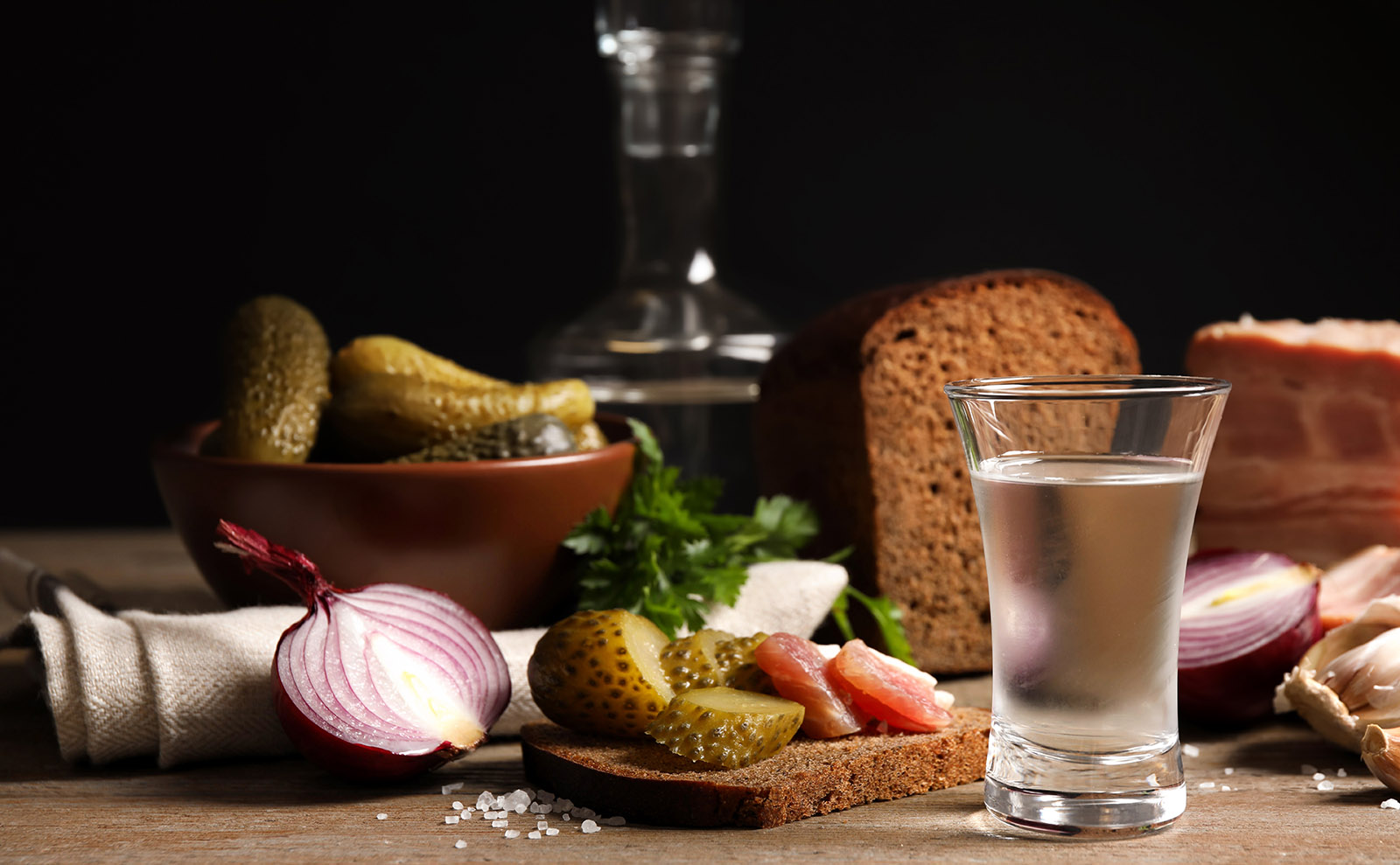 wooden table set with vodka, brown bread, meat, and pickles