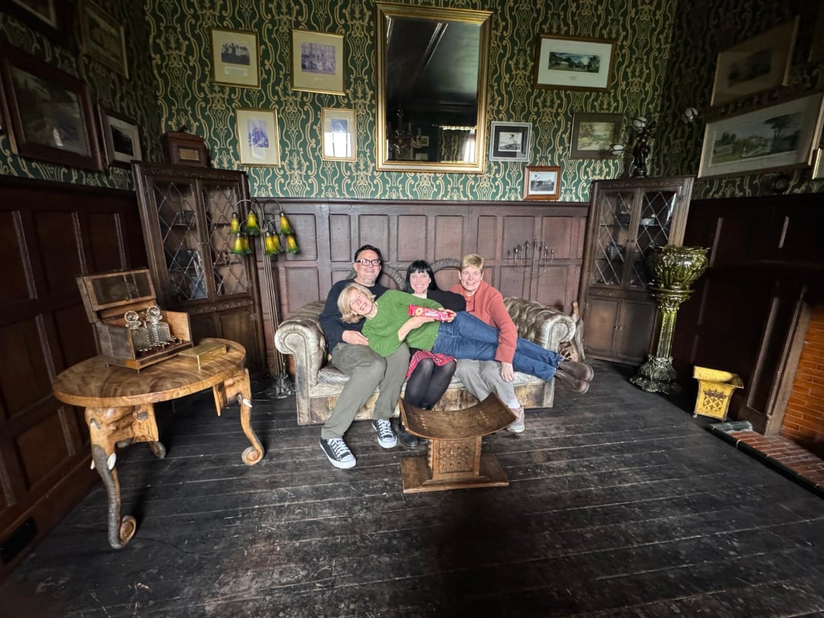 four people sitting on a couch in a room with hardwood floors